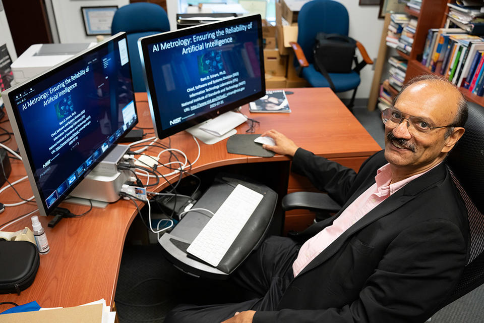 Ram Sriram sits back in his desk chair, smiling. His two computer screens show a slide about AI metrology. 