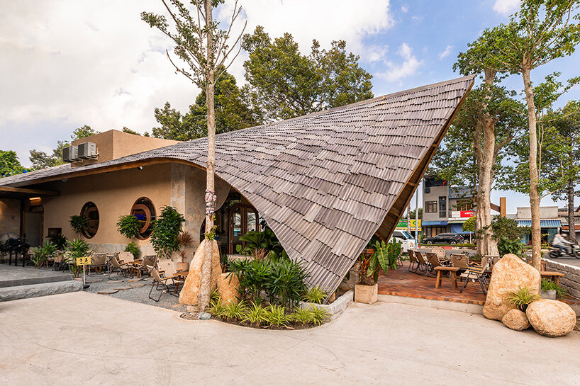 rippling metal roof drapes over interlocking stone volumes of vietnamese café