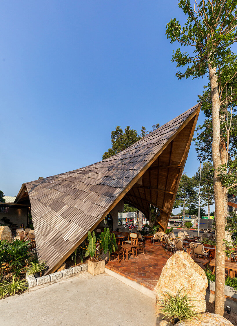 rippling metal roof drapes over interlocking stone volumes of vietnamese café