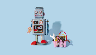 Studio shot of vintage robot toy standing by miniature shopping basket filled with electronic equipment