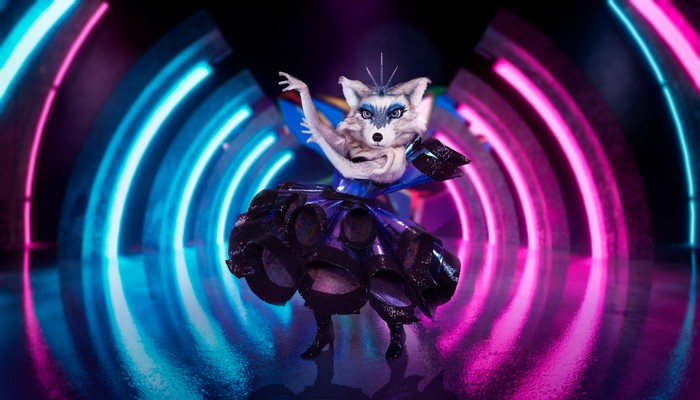 Someone dressed as an Arctic Fox in a dress, raising their arms to one side.