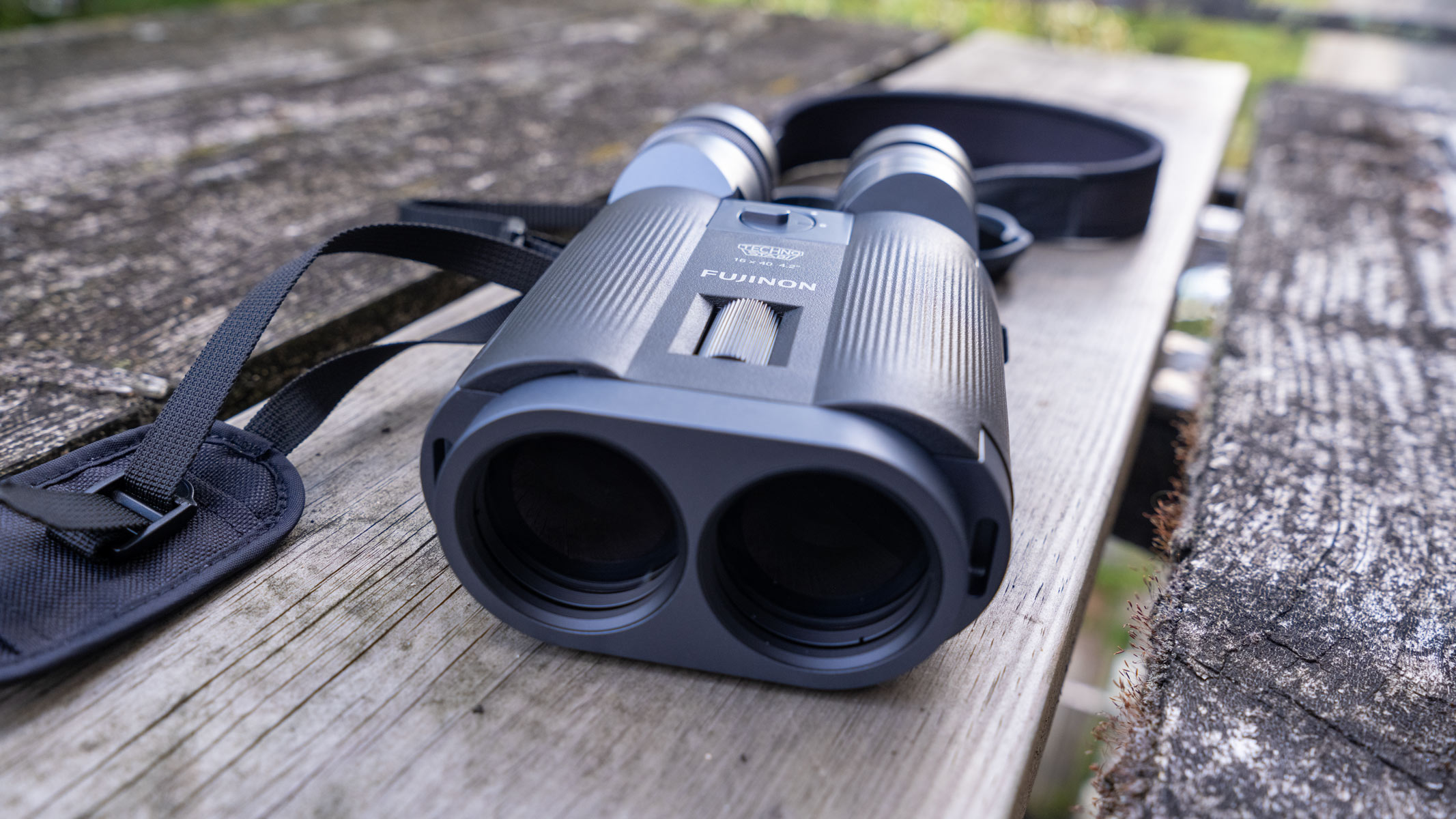 A head-on view of the lenses on the Fujifilm Techno-Stabi TS-L 1640 image-stabilized binoculars on some wooden planks.