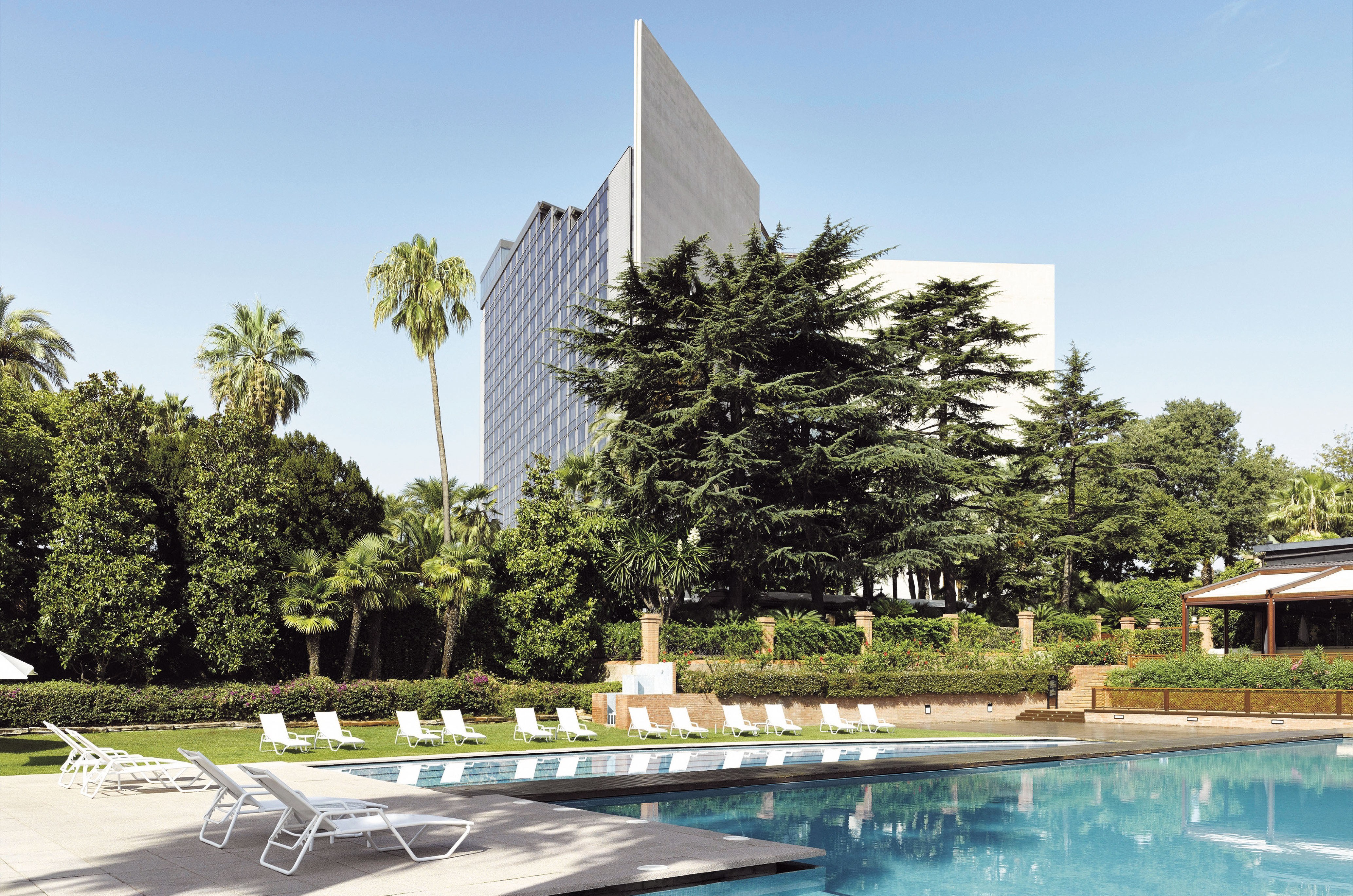 Torre Melina Gran Meliá with a swimming pool and lounging chairs, surrounded by lush greenery and palm trees.