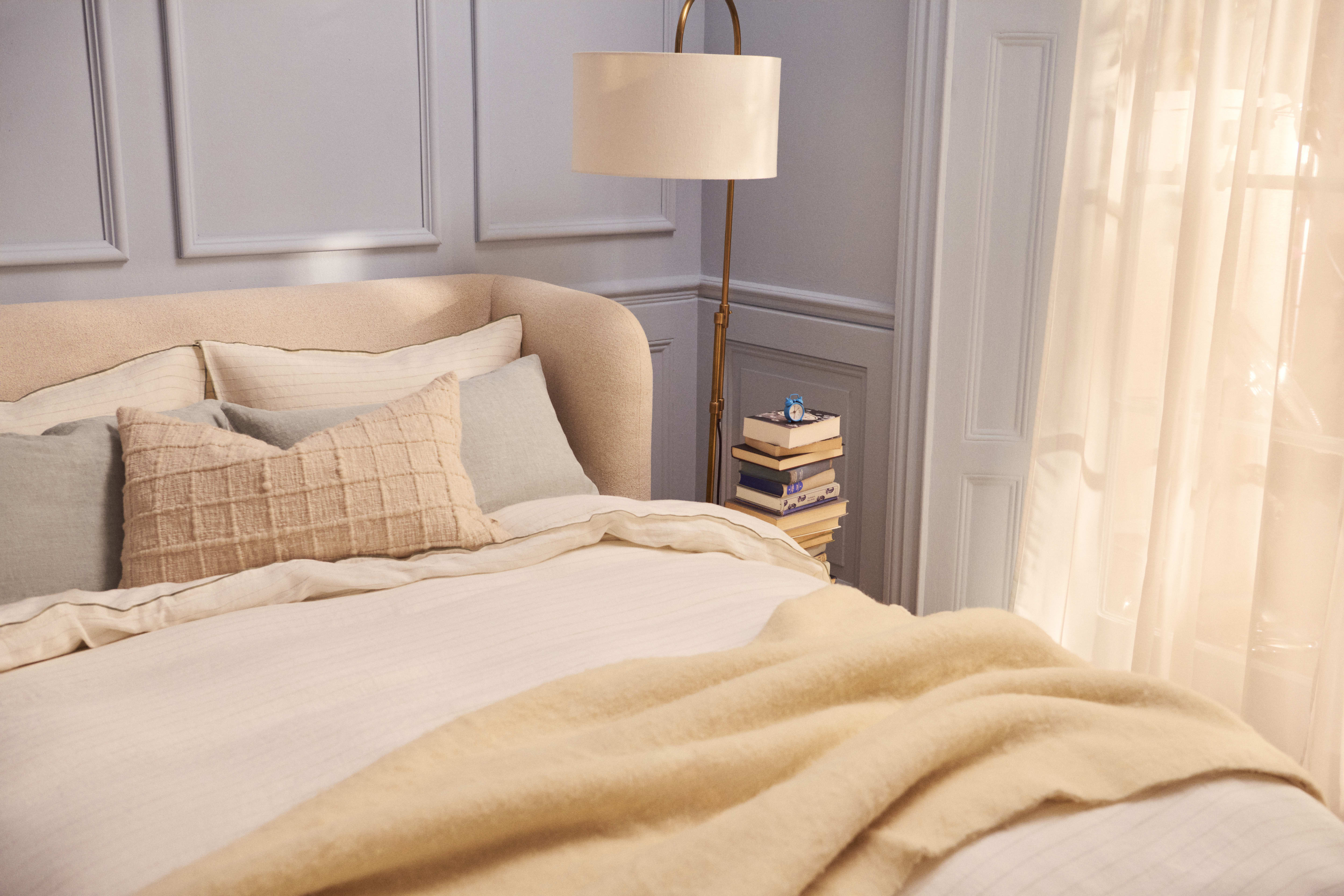 A bed with a Snoozeliner Double Headboard in Whipped Cream Clever Boucle, a cream blanket, and pillows of various sizes.