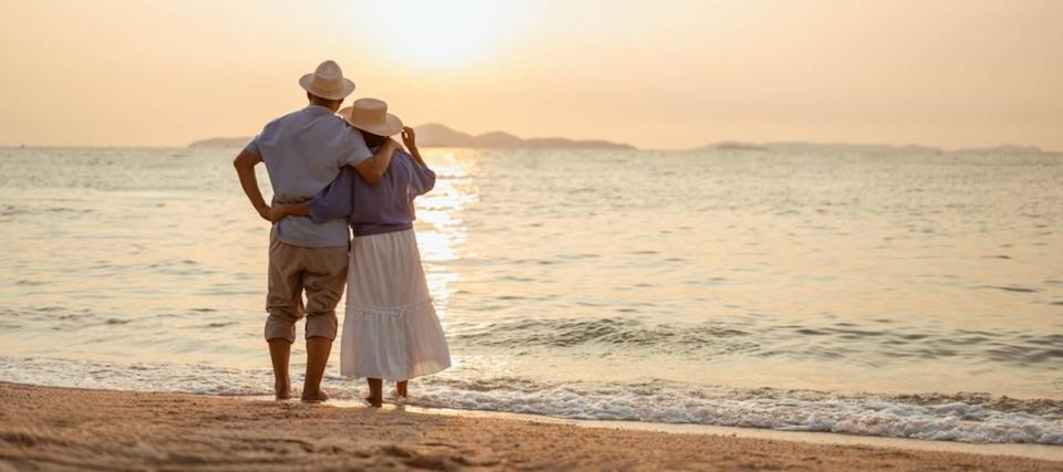 A retired couple standing on the beach at sunset.