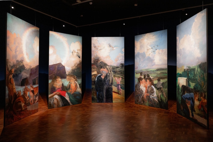 In a dark gallery space hangs five linen panels, painted with detailed scenes of country life, including women and foxes.