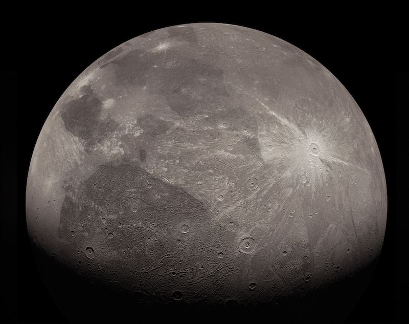 Cratered, moon-like dark and light gray sphere with one bright white crater with rays.