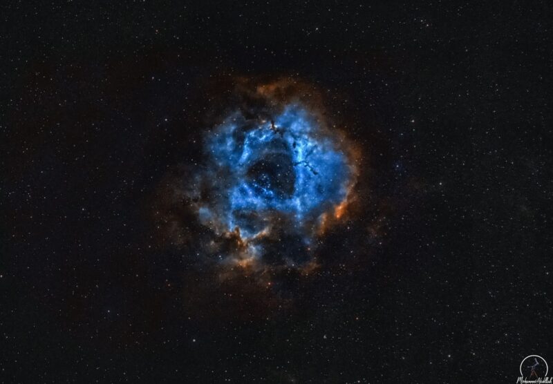 A large, spherical and hollowed-out cloud of blue and orange gas, with a multitude of immersed stars.