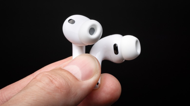 A hand holding a pair of AirPods Pro 3 over a black background