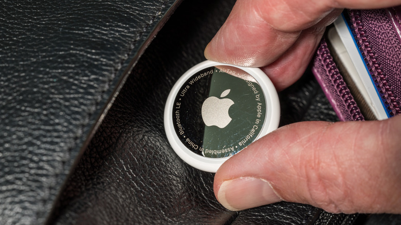 a hand putting an AirTag into a leather pocket