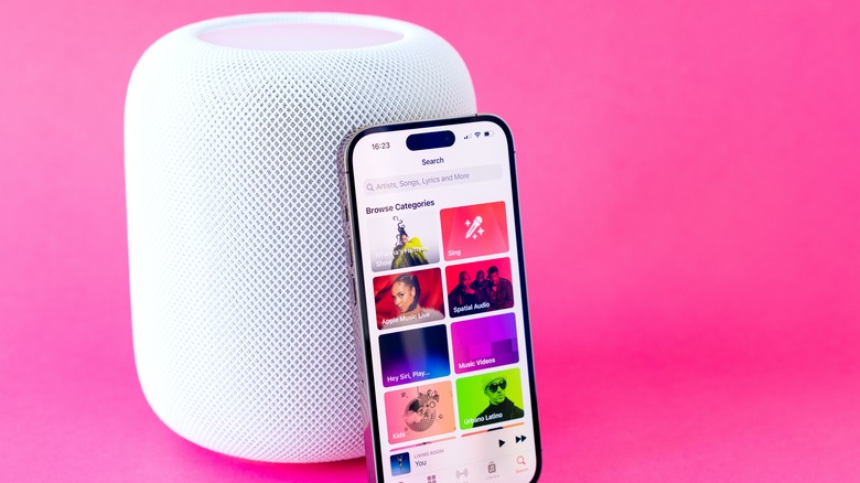 An Apple HomePod with an iPhone leaning against it, pink background