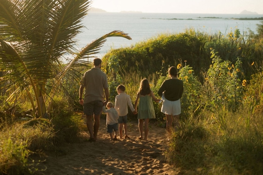 Family of six walk through nature down to the beach.