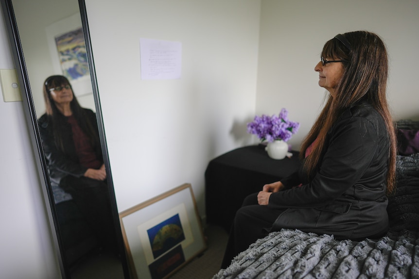 Jane Turner sits on her bed in front of a mirror