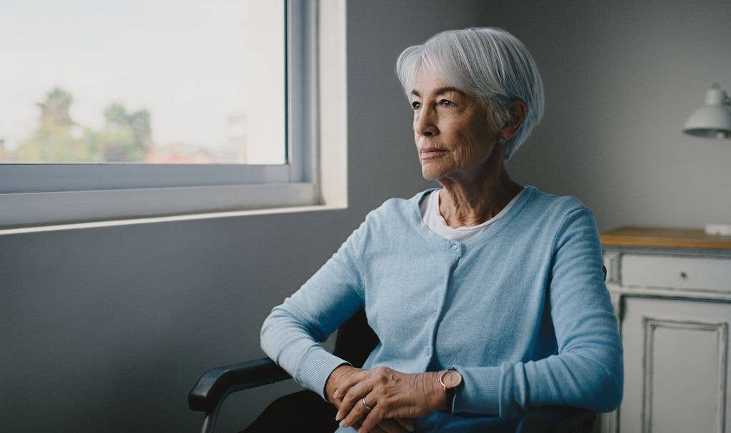 Senior woman with short grey hair wearing a blue cardigan wheelchair in a care home with Alzheimer, dementia