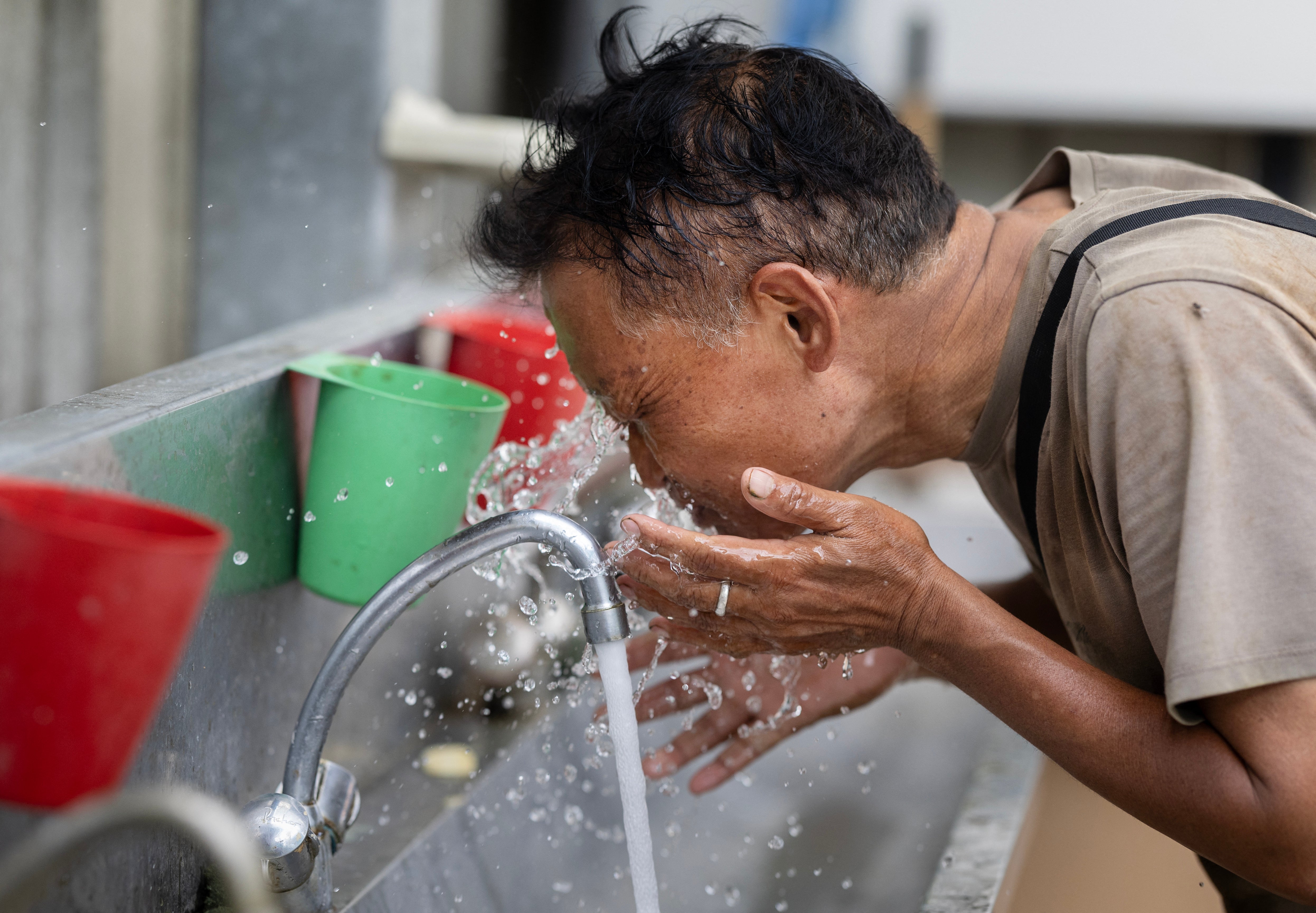An employee puts water on his face as he works in a greenhouse of tomatoes in Taule, western Franc