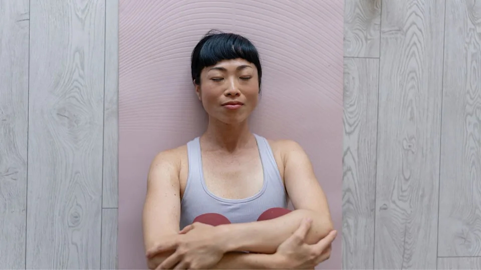 Woman doing Pilates toe taps lying on yoga mat on wooden floor.