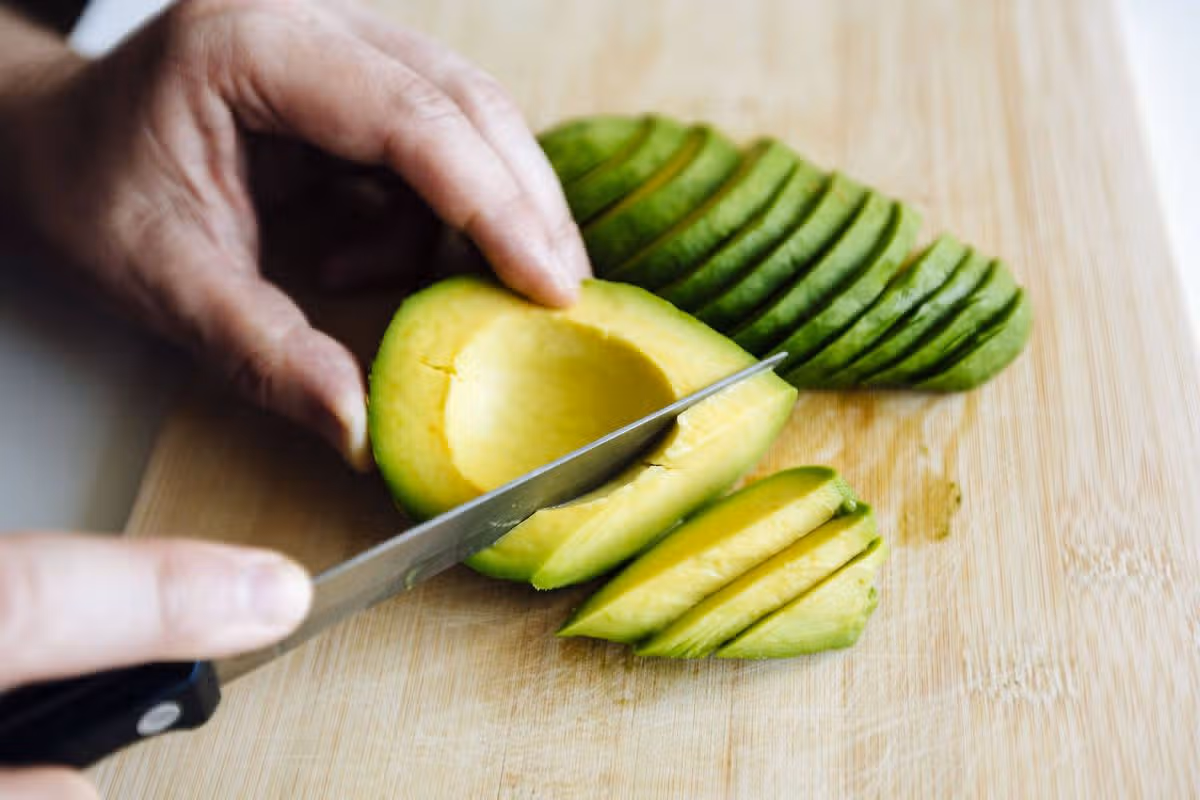 Man slicing avocado with a knife on a cutting board close up