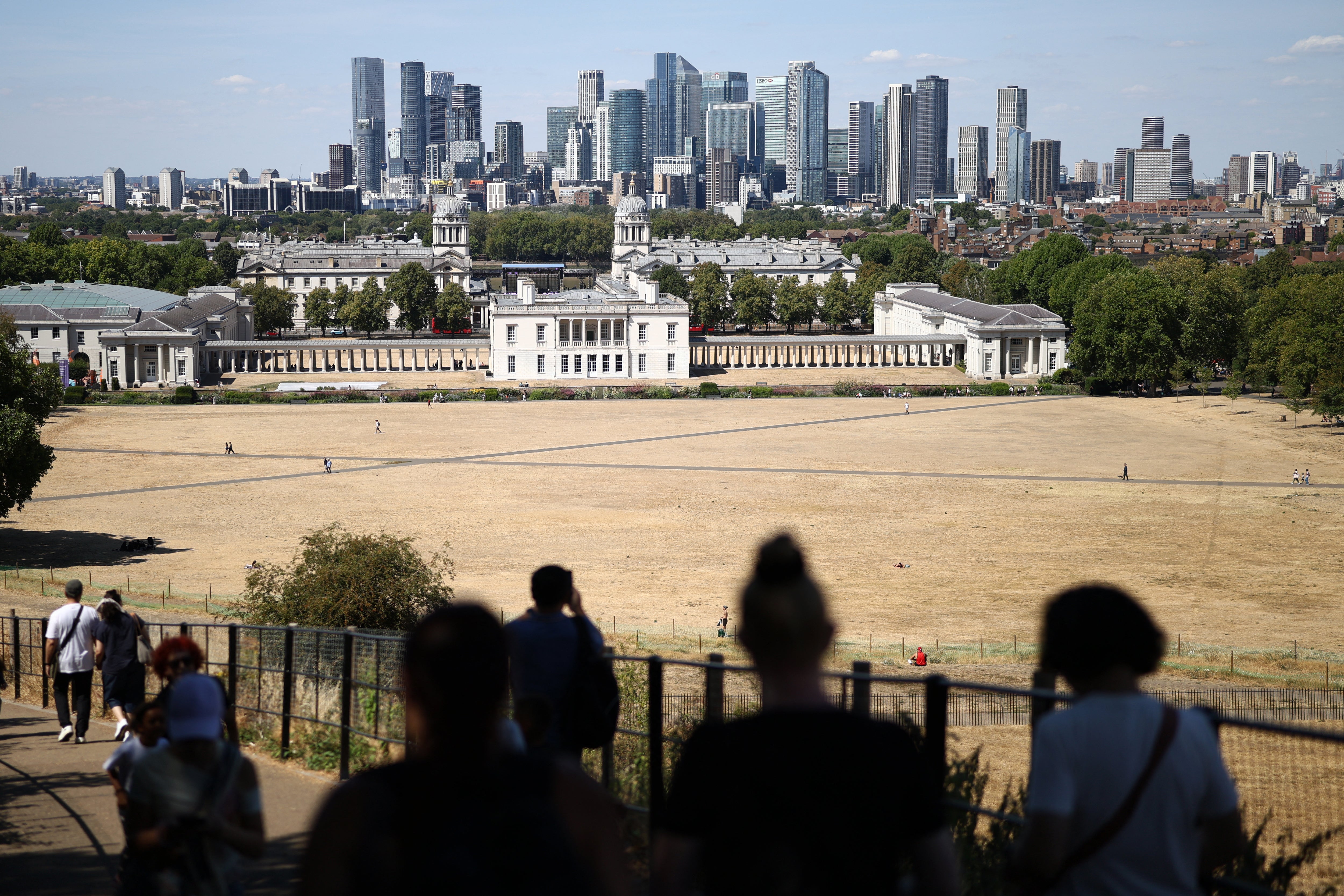 People walk on a path between the sun-scorched grass, turned yellow-brown by a lack of rain, in London’s Greenwich Park