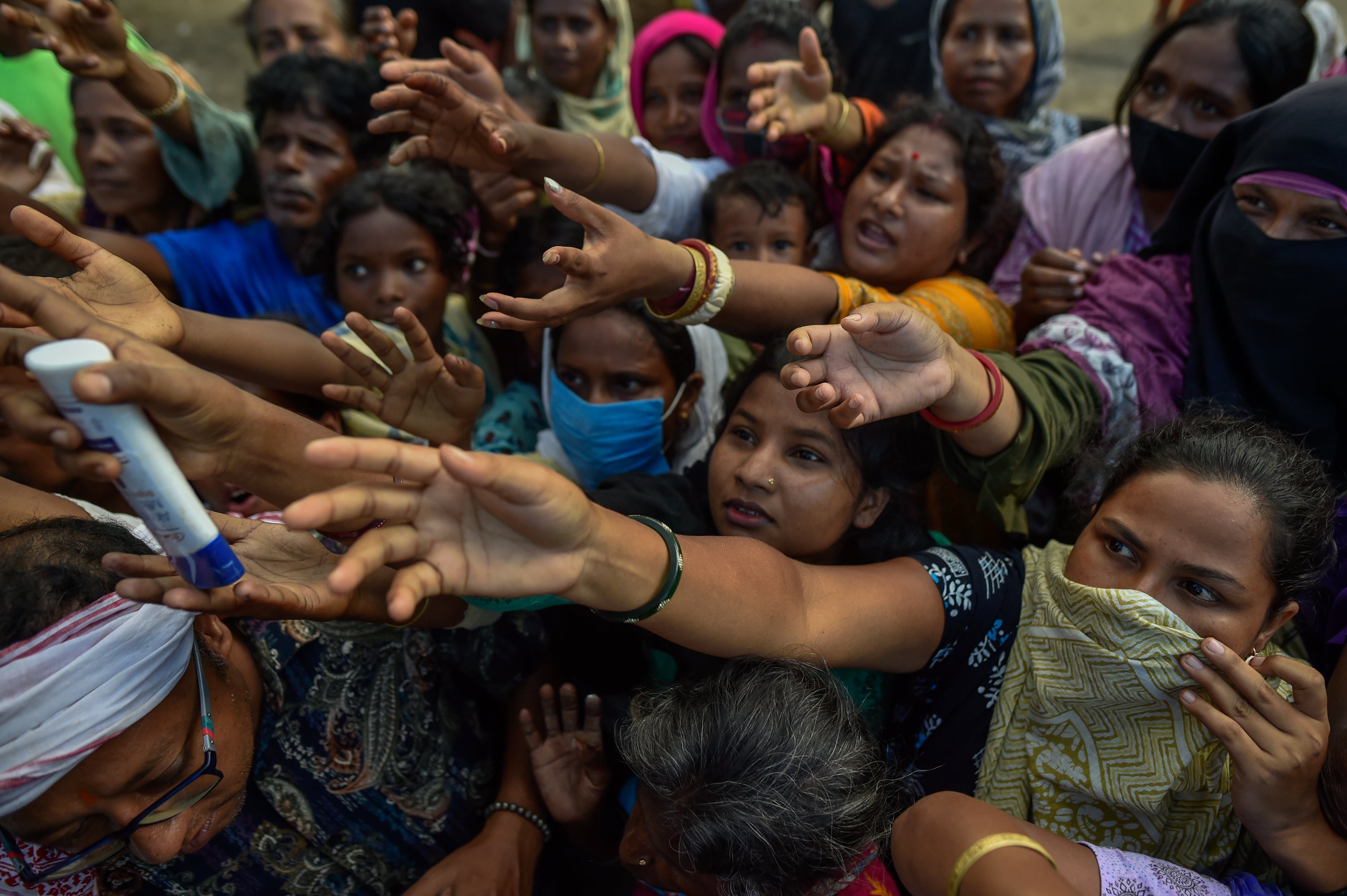 Flood affected residents reach out to receive relief supplies during a distribution at a temporary relief camp on August 05, 2026 in Sivasagar, Assam, India