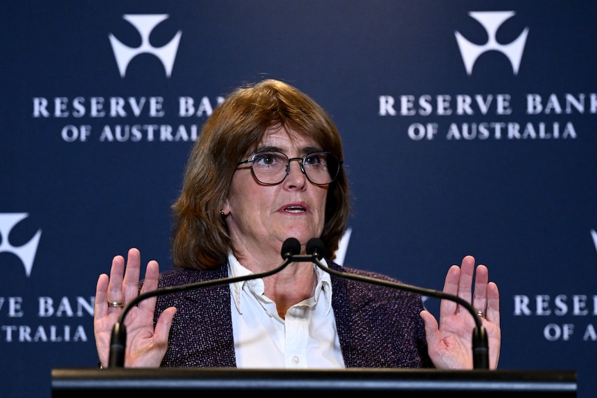 Michele Bullock at lectern, with hands raised