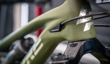 Close-up of a bicycle frame with a green finish, featuring a Lapierre branding badge. The frame shows water droplets, suggesting recent exposure to moisture. Blurred background indicates a workshop or garage setting.