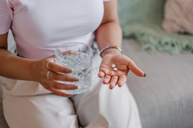 Beautiful young Indian woman taking medicine pills with a glass of water. Close-up.