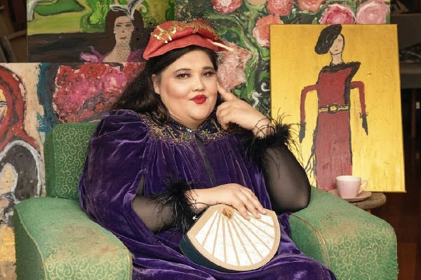 A woman sitting surrounded by her bold, bright paintings.