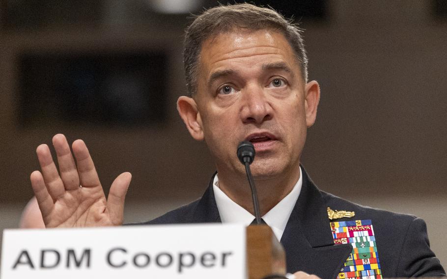 Cooper, nametag in front him, gestures with his right hand as he testifies.