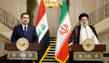 Two officials at podiums with Iraqi and Iranian flags during diplomatic meeting