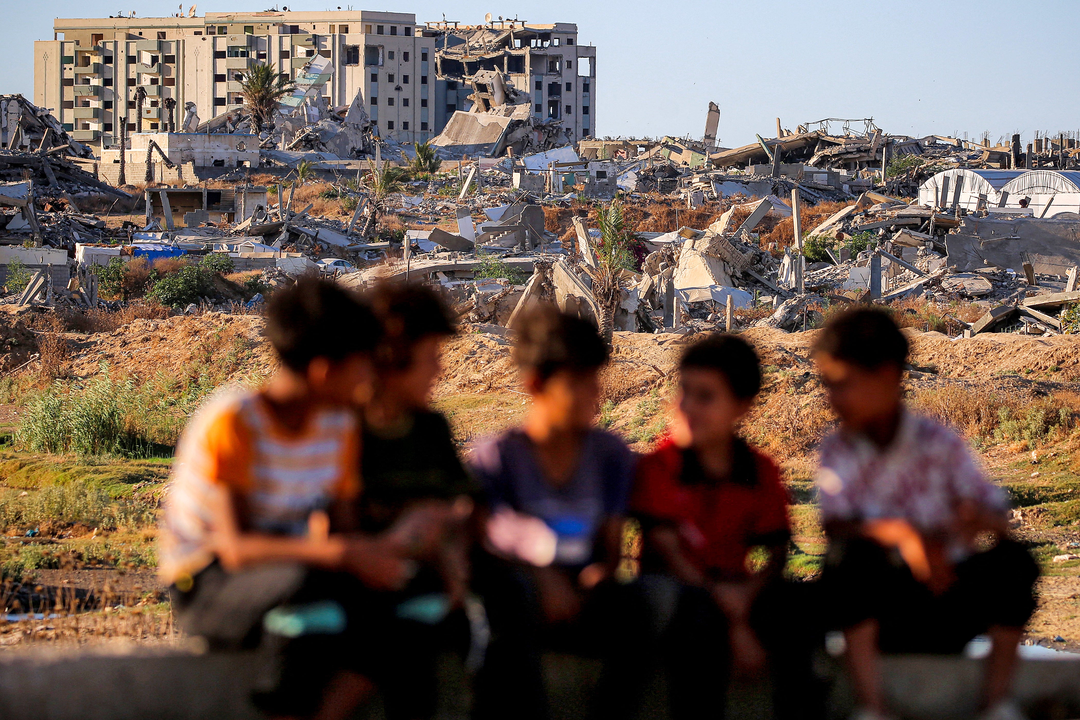 Children sit together near destroyed and heavily-damaged buildings at the Nuseirat camp for Palestinian refugees in the central Gaza Strip on June 19, 2026.