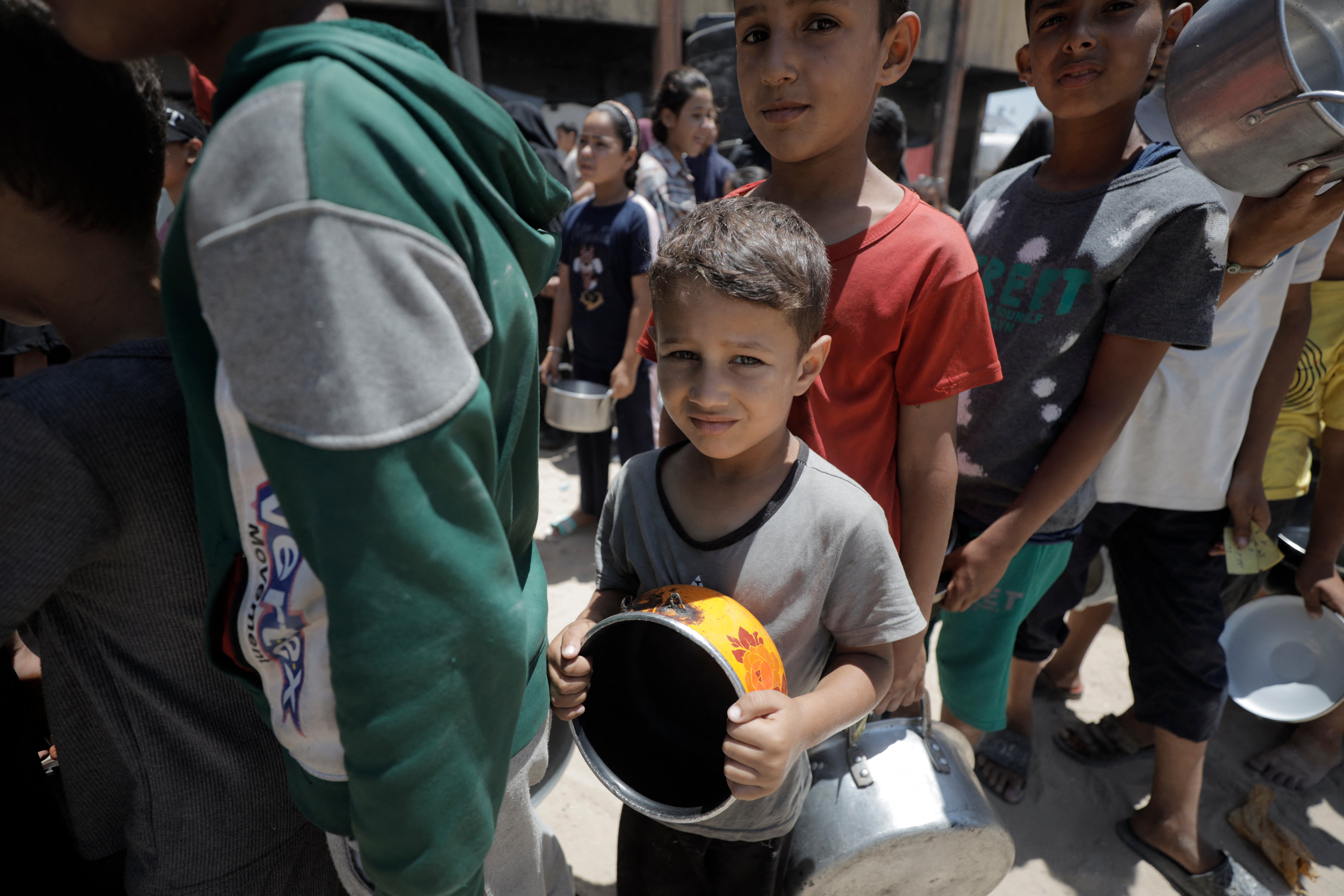 Displaced Palestinian children carrying cooking pots stand in a line to receive aid in the grounds of al-Faluja School in Jabalia refugee camp in the northern Gaza Strip