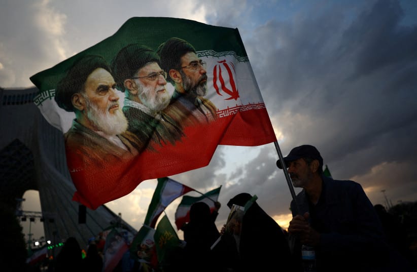 A MAN holds a flag with a picture of late leader of the Islamic Revolution Ayatollah Ruhollah Khomeini, late supreme leader Ayatollah Ali Khamenei, and Iran’s new Supreme Leader Mojtaba Khamenei, during a rally in Tehran, in April 2026.