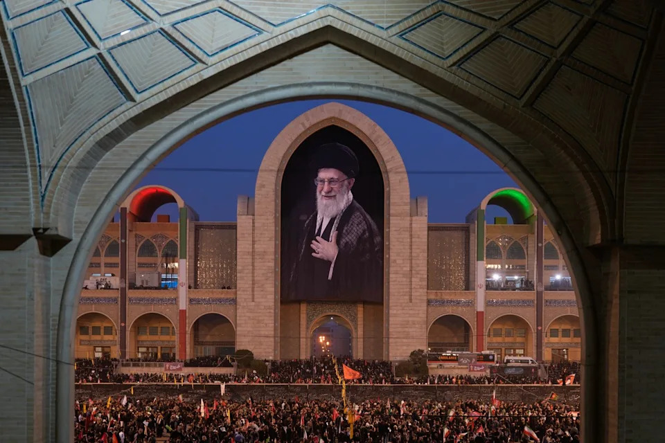 Mourners gather beneath a portrait of the late Iranian Supreme Leader Ayatollah Ali Khamenei during the funeral ceremonies for Khamenei and members of his family at the Imam Khomeini Mosalla Grand Mosque in Tehran, Iran, Saturday, July 4, 2026. (AP Photo/Altaf Qadri) - The Associated Press