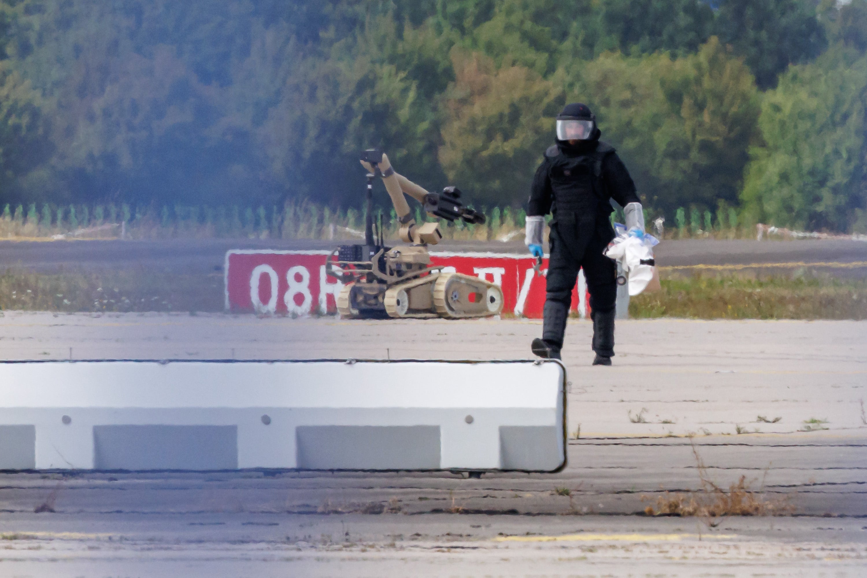A police investigator works on the tarmac with a robot capable of defusing explosives