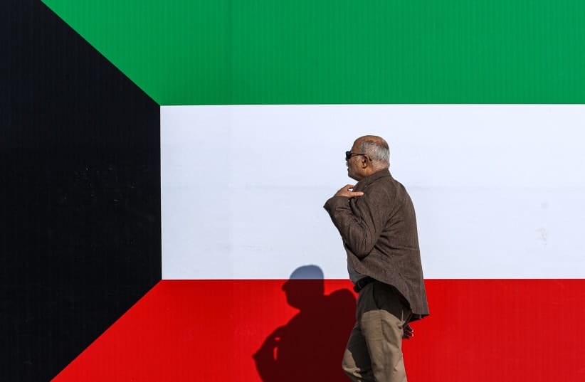 A man walks along the pavement next to a large banner depicting the flag of Kuwait.