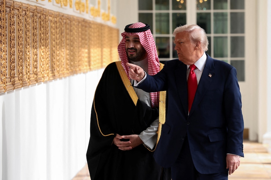 Donald Trump points at a wall while walking with Mohammed bin Salman.