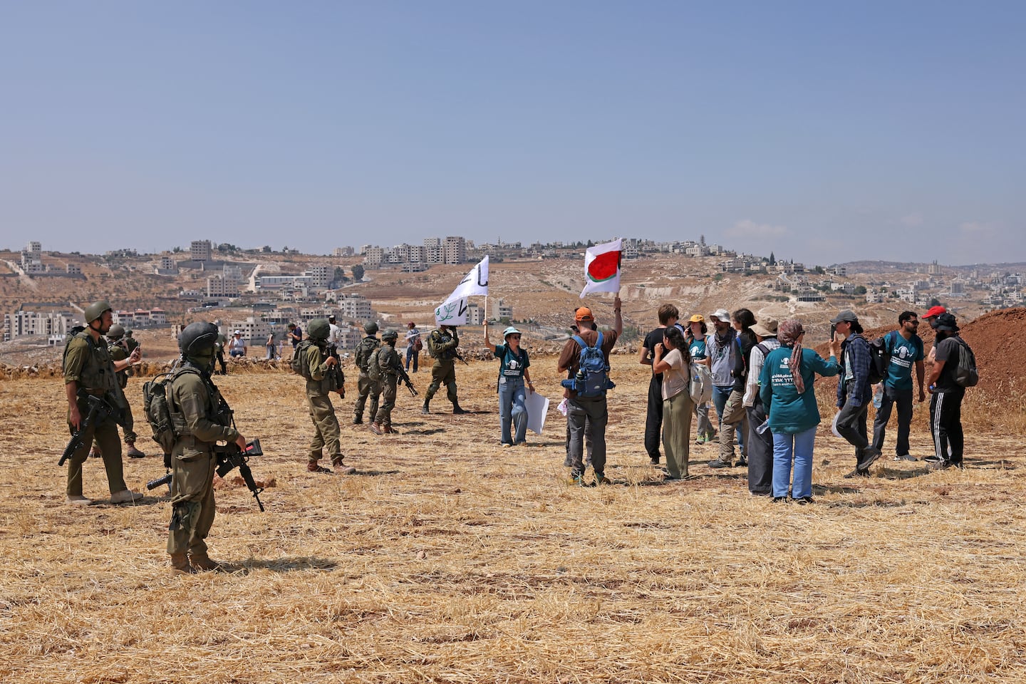 Activists hold flags next to Israeli soldiers as they accompany Palestinian landowners to their property, which is at risk of being confiscated by Israeli settlers, in Beit Sahur, south of Bethlehem, in the occupied West Bank on Aug. 14, 2026. Violence against Palestinians by Israeli settlers in the West Bank has increased dramatically since the Oct. 7, 2023 attack on Israel by Hamas from the Gaza Strip. More than 500,000 Israelis live in settlements in the West Bank, which are illegal under international law, among some three million Palestinians in the territory.