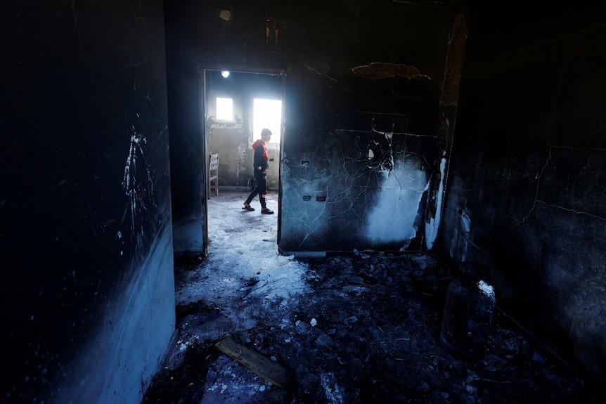 A young boy walks in a dark, damaged building.