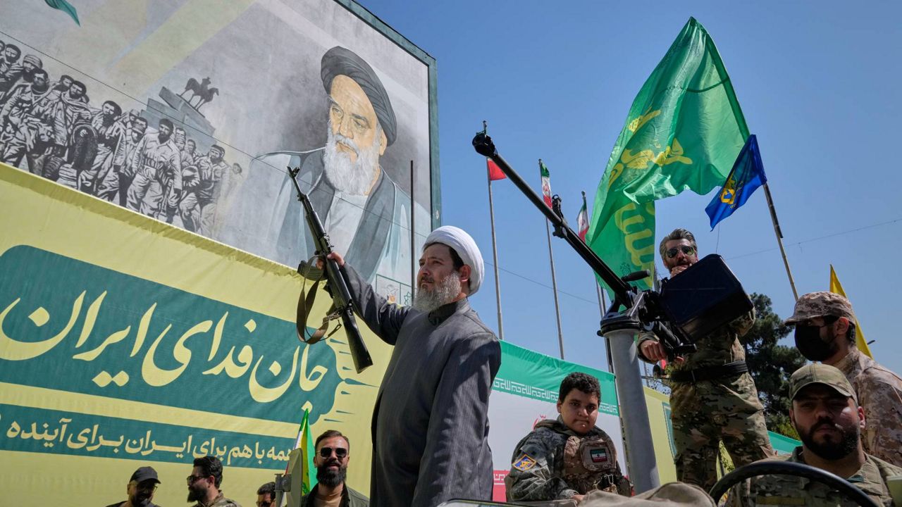 An armed Shiite cleric rides aboard a military vehicle past a billboard depicting Ayatollah Ruhollah Khomeini, founder of the Islamic Republic, during the state-organized "Janfada," or "Sacrifice for Iran," military-style parade in Tehran, Iran, Friday, Sept. 18, 2026. (AP Photo/Vahid Salemi)