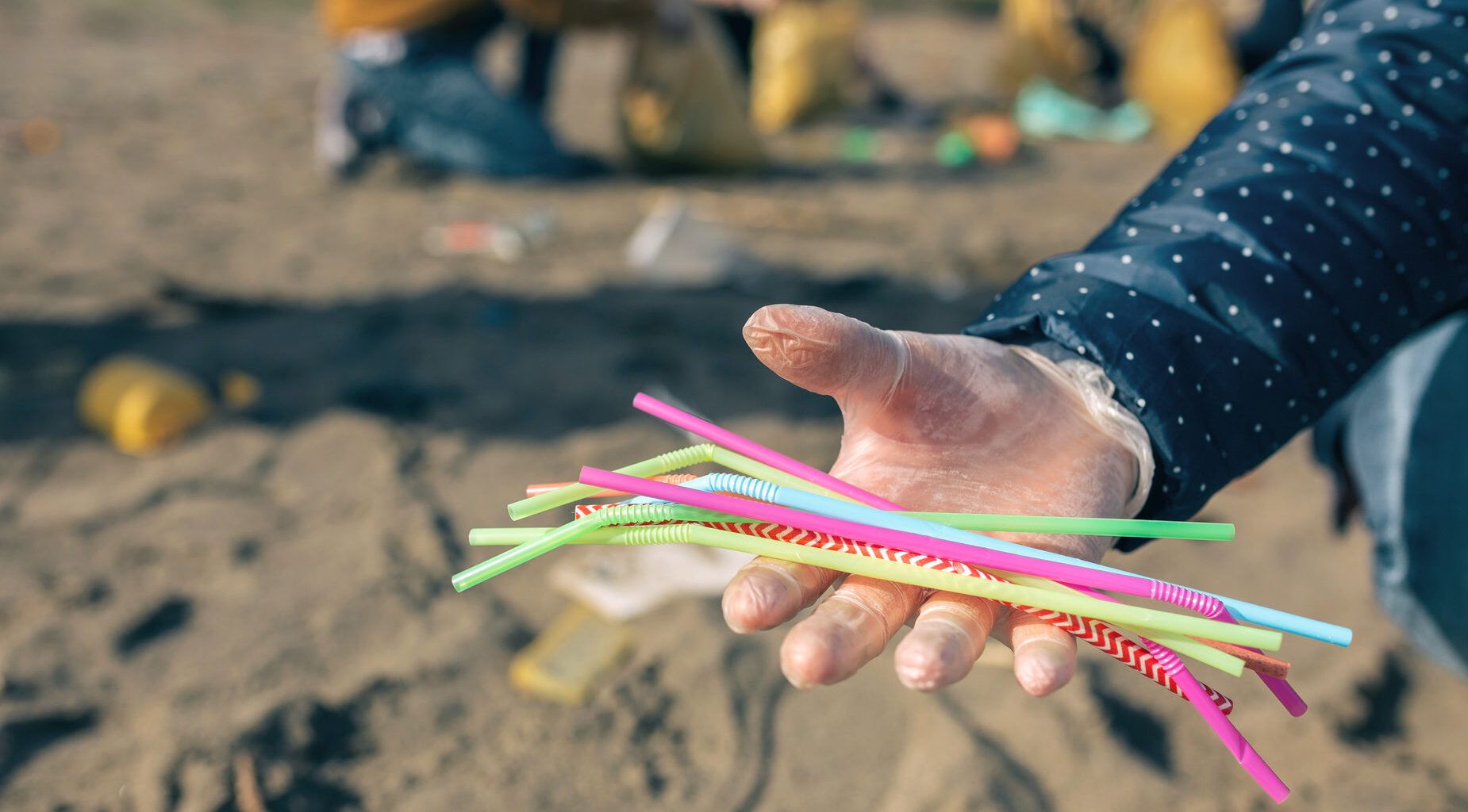 Donna con guanto mostra cannucce di plastica raccolte tra i rifiuti su una spiaggia