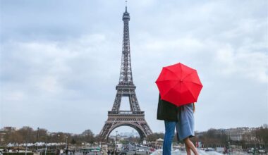 coppia si bacia dietro un ombrello rosso con torre eiffel come sfondo
