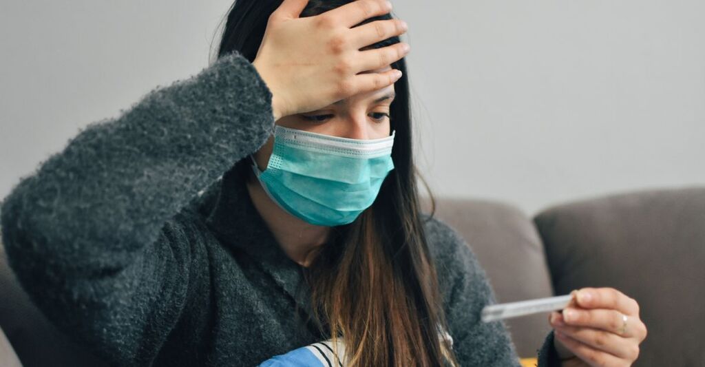 Una donna con mascherina si prova la febbre