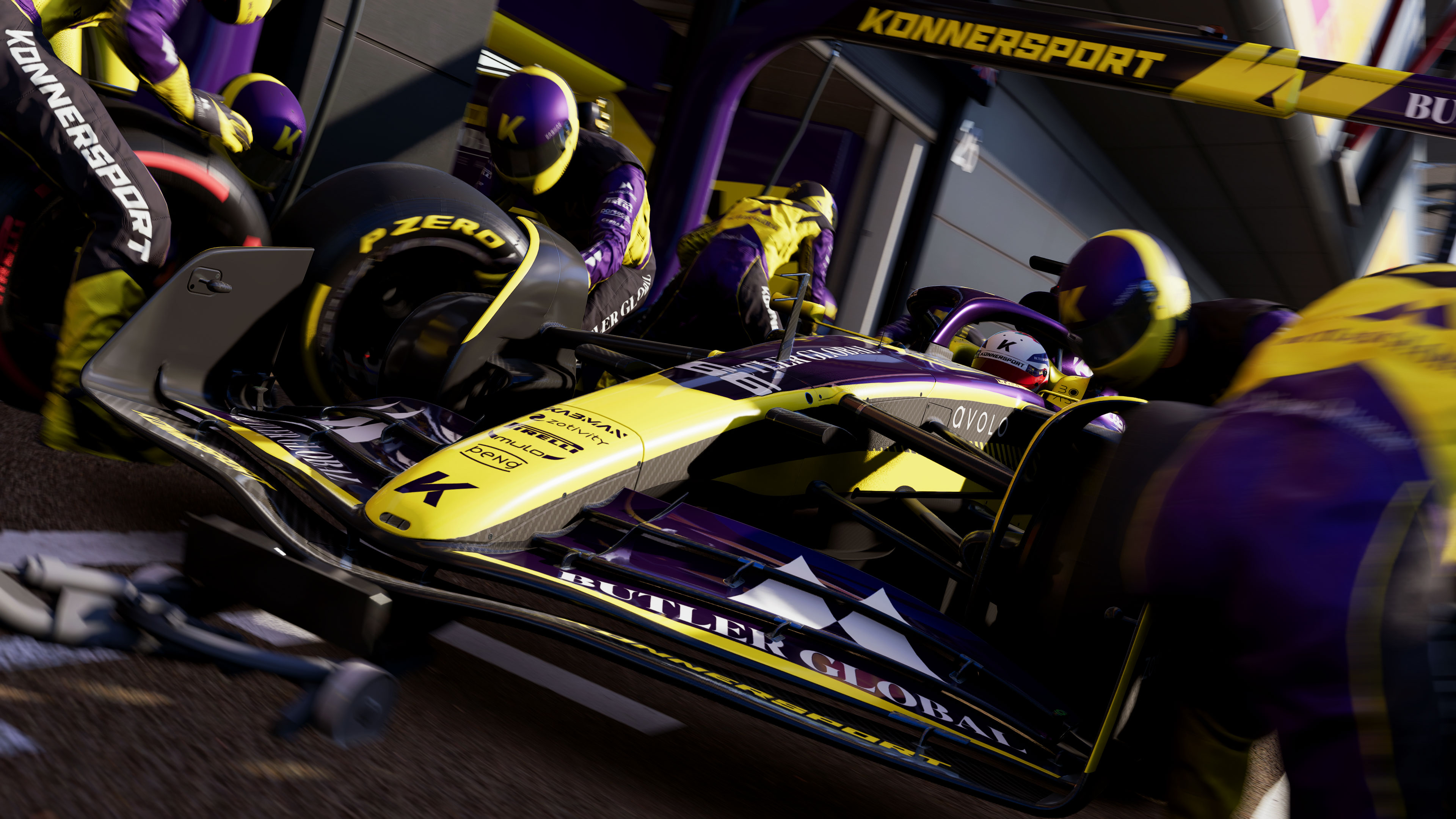 Un'auto di F1 della Konnersport con livrea gialla ferma ai box per un cambio gomme a opera dei meccanici