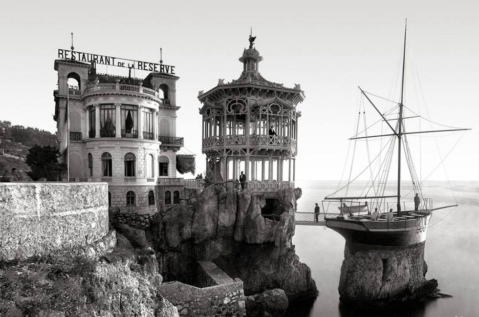 historic coastal restaurant perched on a rocky cliff with a nearby ship