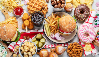 Assortimento di cibo spazzatura visto dall'alto: panini con hamburger, nuggets, pop corn, patatine, waffle, donut glassati, cupcake, marshmallow, ketchup; concept: snack, junk food, ultra processati