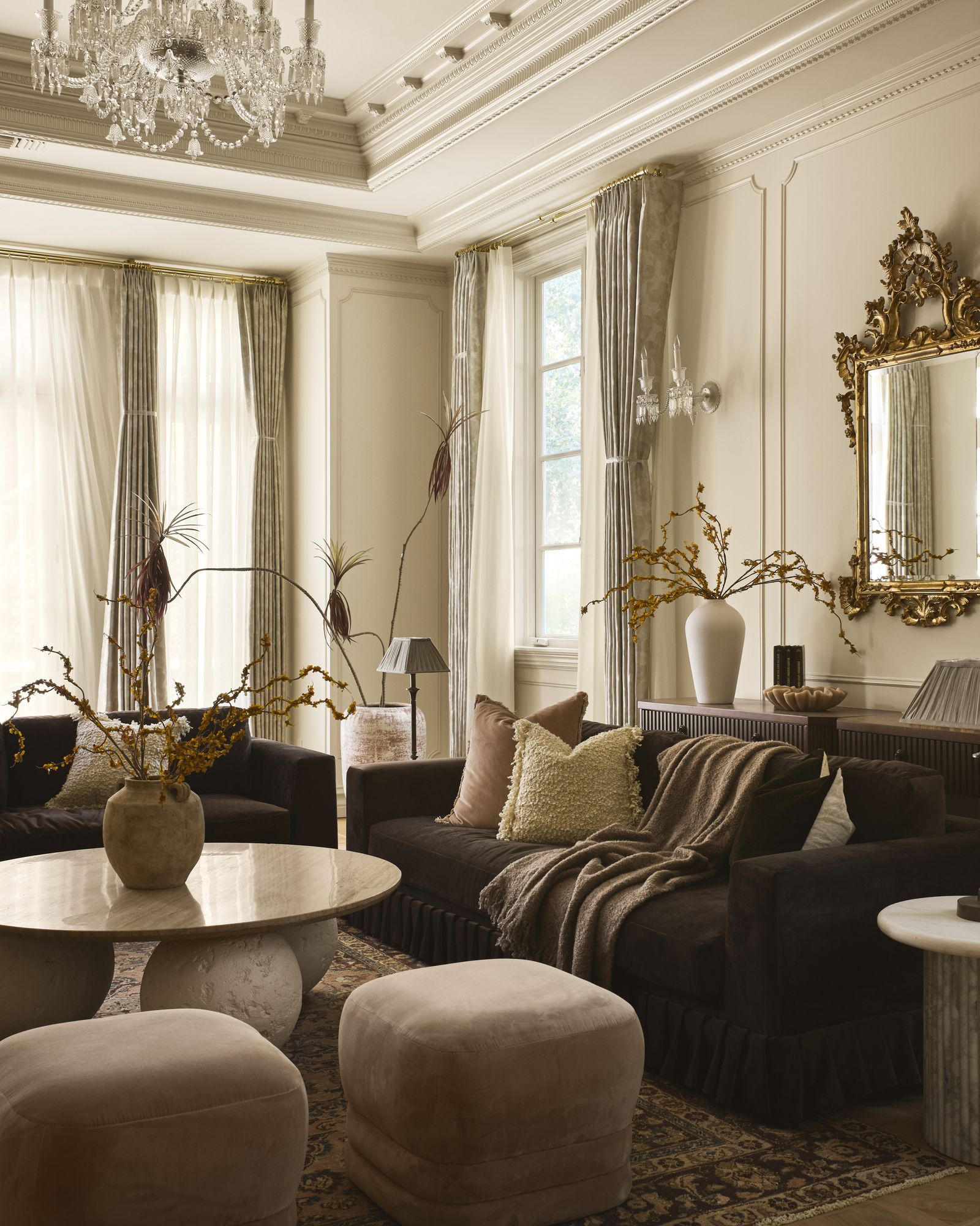 salotto divani marrone scuro  pouf beige tavolino rotondo con piedistallo a sfere specchio antico boiserie tende lampadario