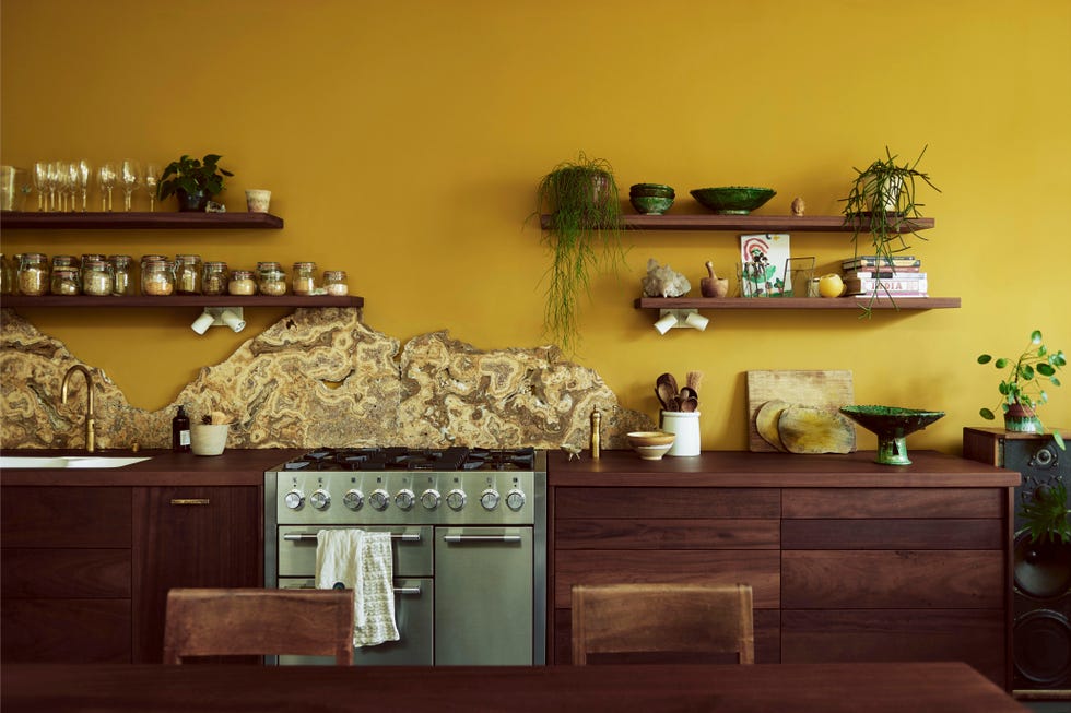 open plan kitchen with rich yellow wall colour and marble splashback above silver oven