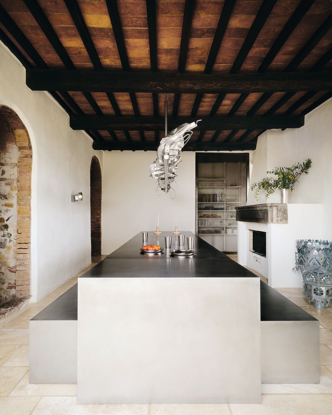 Sala da pranzo tavolo e panche in metallo tetto con travi in legno porte con archi e mattoni camino lampadario in metallo