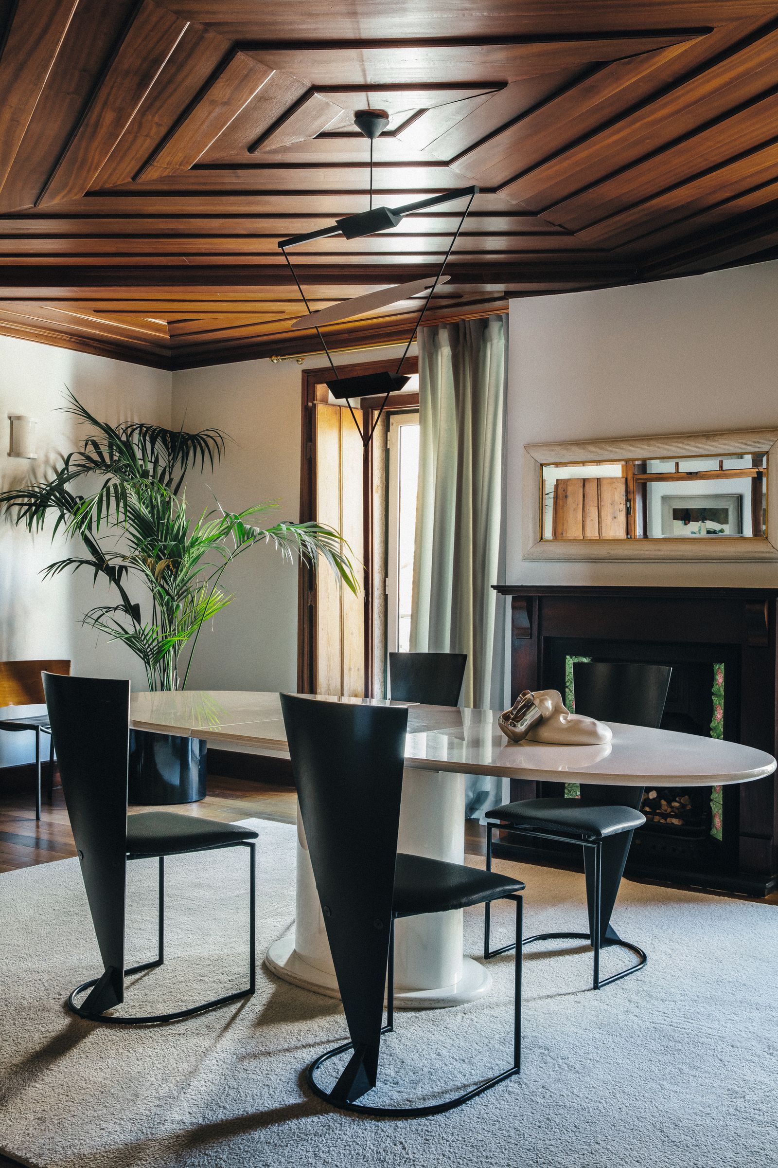 sala da pranzo tavolo ovale in marmo sedie nere soffitto in legno lampadario pianta camino specchio
