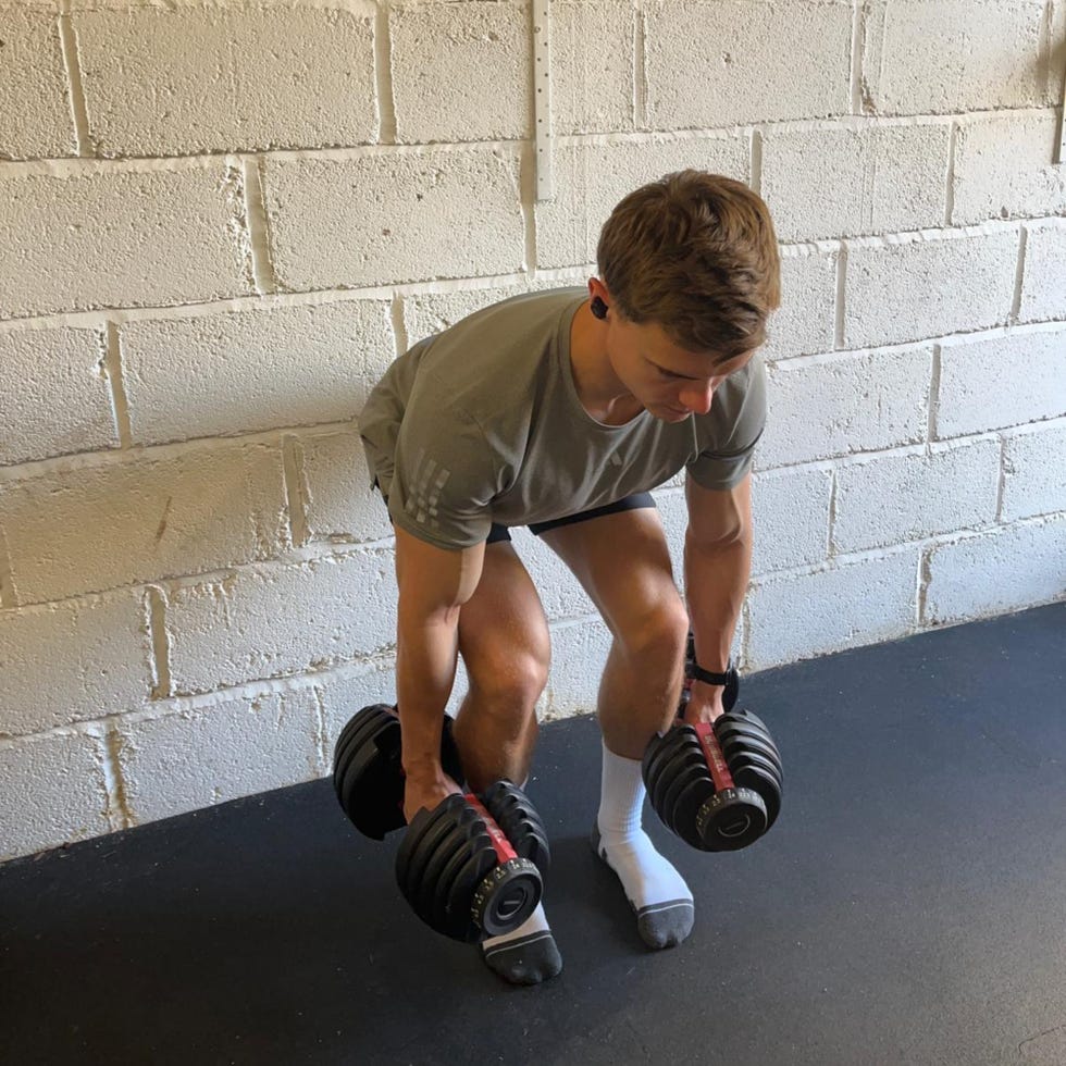 person performing a deadlift with dumbbells in a gym